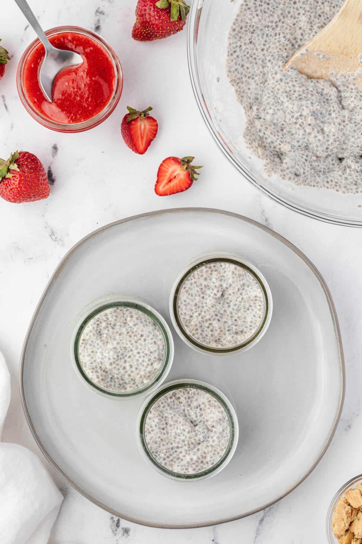 Adding a layer of coconut cheesecake chia pudding to individual glass serving jars.
