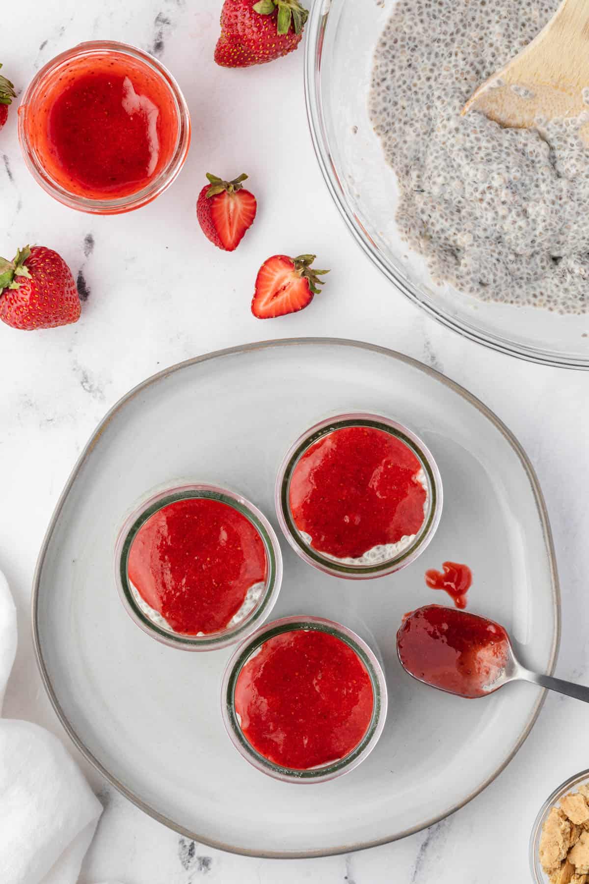 Adding a strawberry sauce layer to jars of coconut cheesecake chia pudding.
