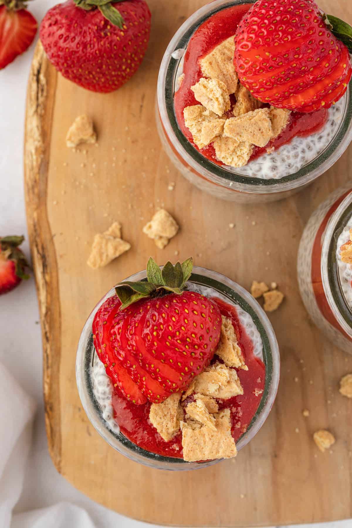 An overhead image of jars of cheesecake chia pudding topped with strawberries and graham crackers.