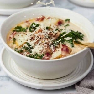 A bowl of zuppa toscana with parmesan cheese being sprinkled on top.
