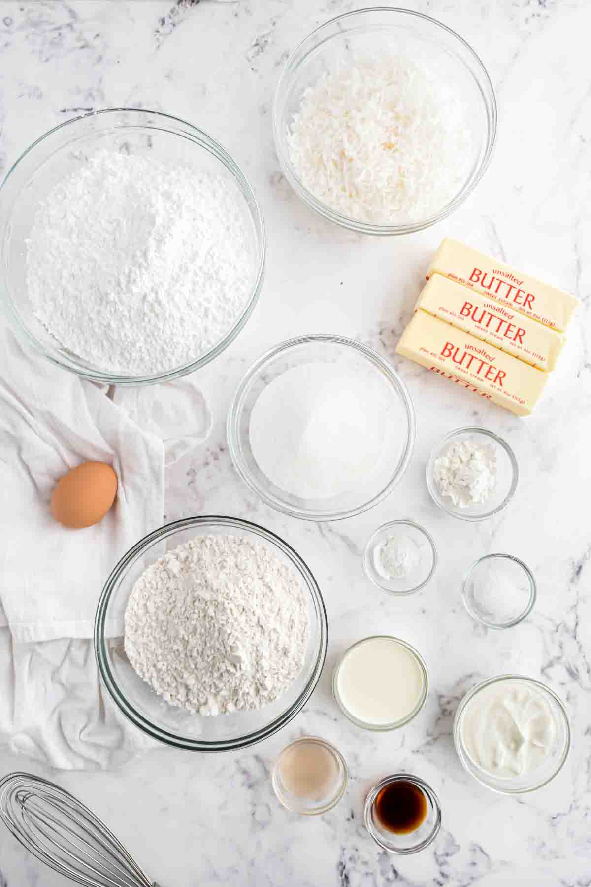 Ingredients for frosted coconut sugar cookie bars in separate bowls on a white marble surface.