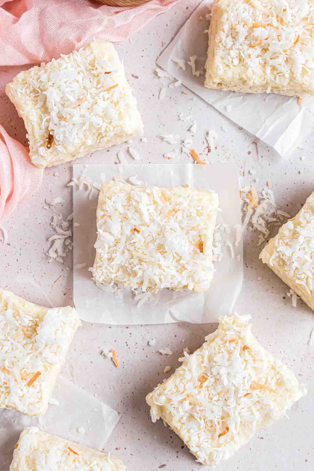 Frosted coconut sugar cookie bars with sweetened shredded coconut sprinkled on top and around them.