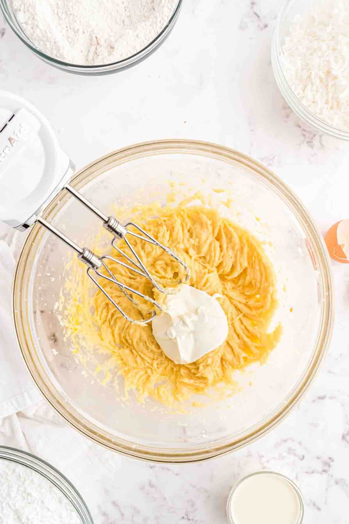 Adding sour cream to cookie dough in a mixing bowl.