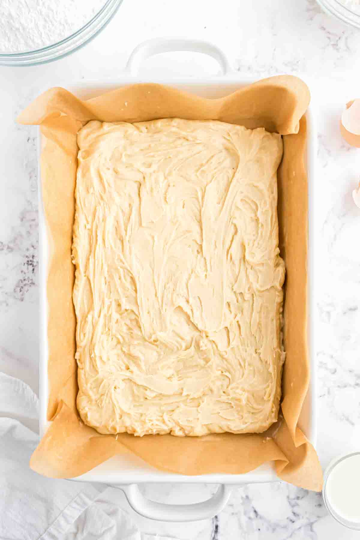 Sugar cookie dough spread into a white baking dish lined with a parchment paper sling.