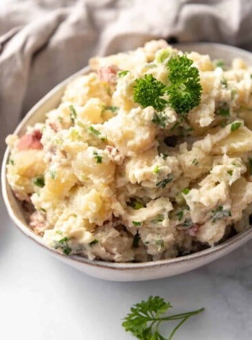 A serving bowl filled with Greek potato salad with sprigs of fresh parsley.
