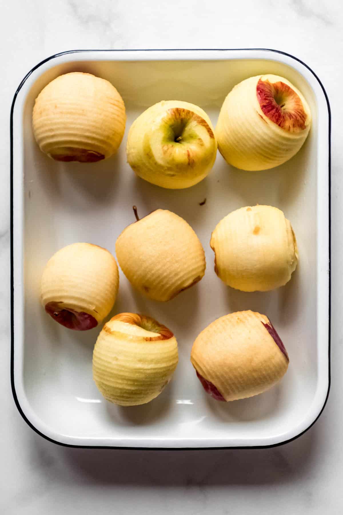 Several peeled apples in a baking dish.