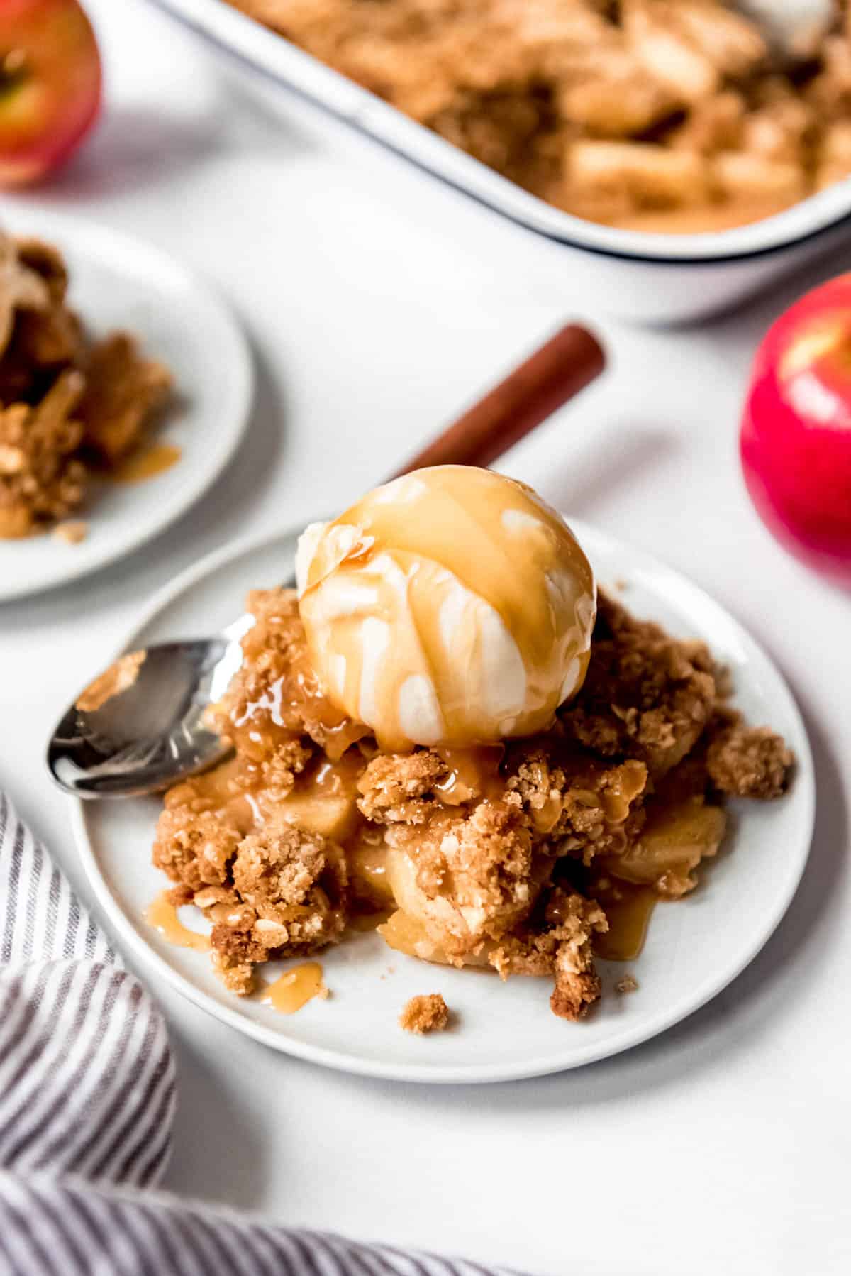 A serving of apple crisp on a dessert plate with ice cream and caramel syrup on top.