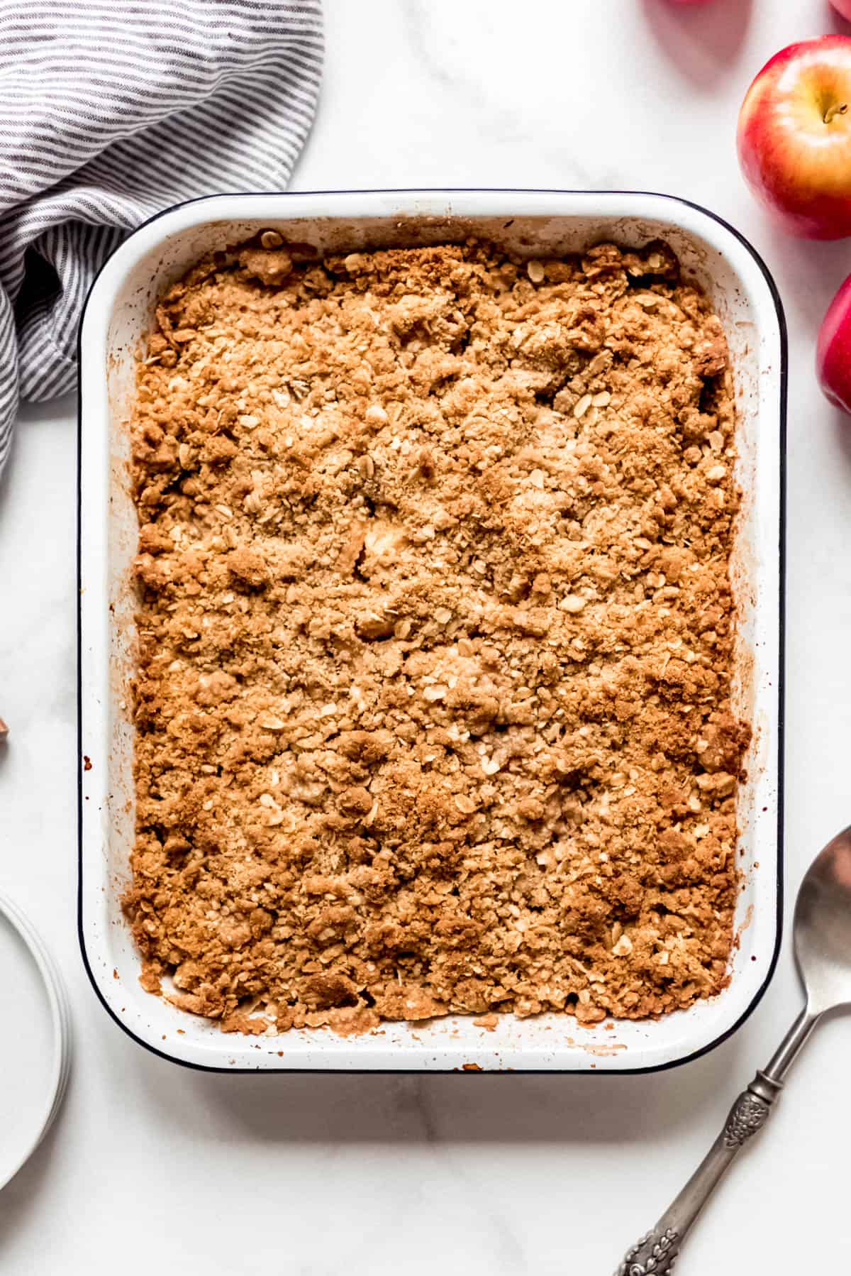 A baked apple crisp next to red apples.