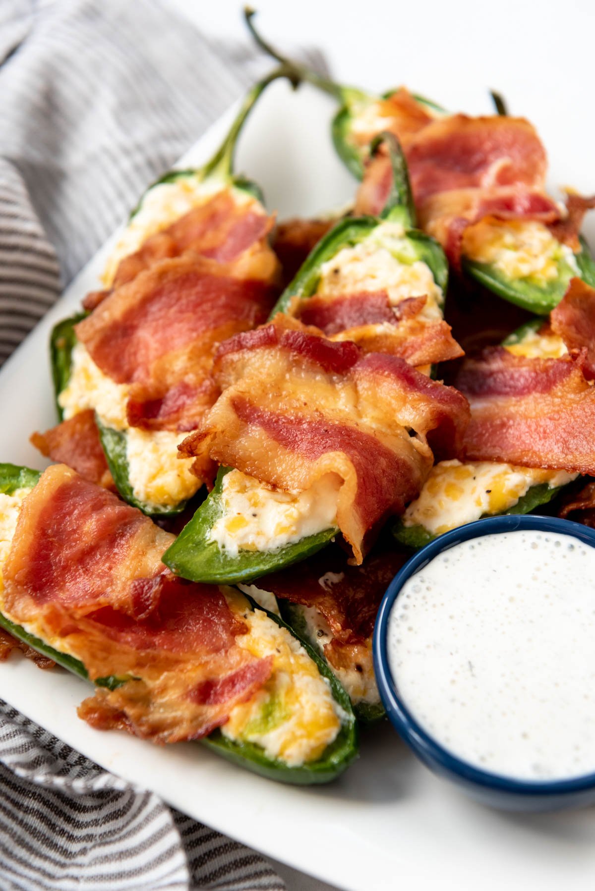 Bacon wrapped jalapeno poppers on a plate with ranch dipping sauce.