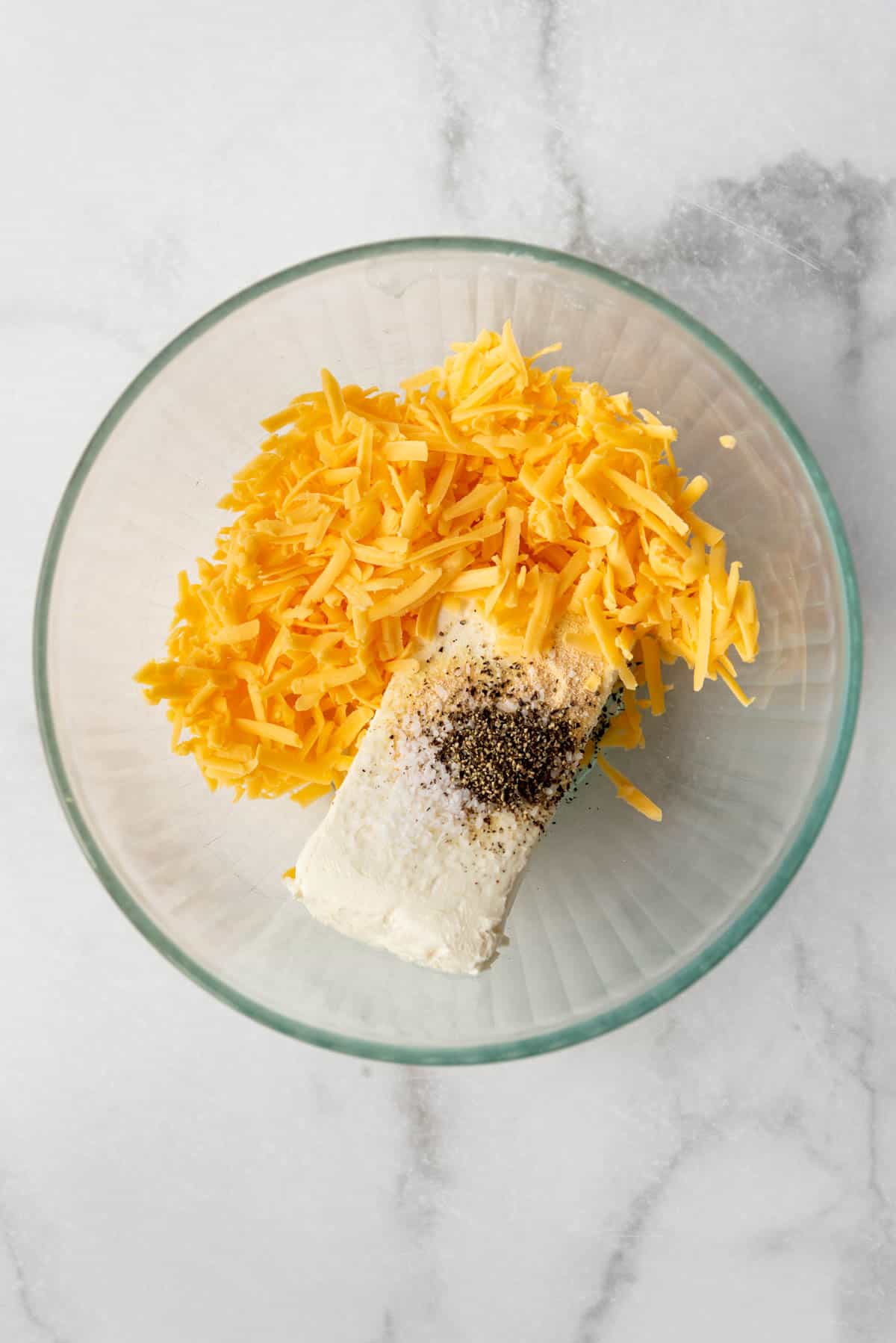 A bowl with cream cheese, cheddar cheese, salt and pepper.