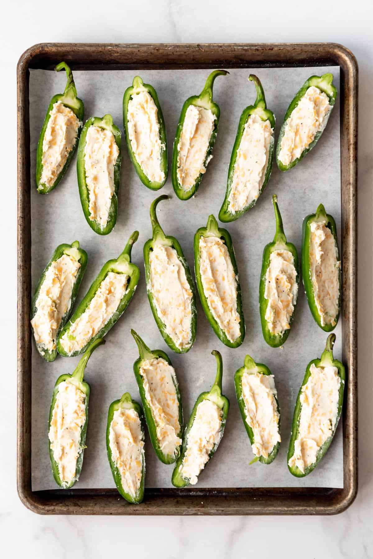 Jalapeno halves with cream cheese and cheddar cheese filling on a baking sheet.