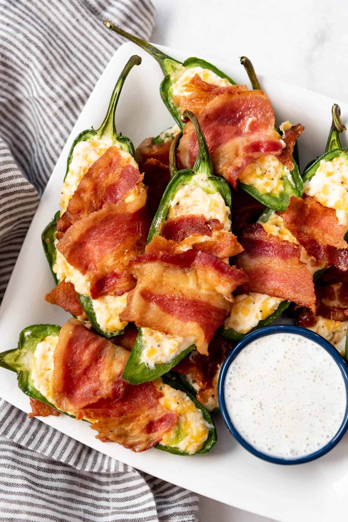 Homemade jalapeno poppers wrapped in bacon on a plate with ranch dressing on the side.