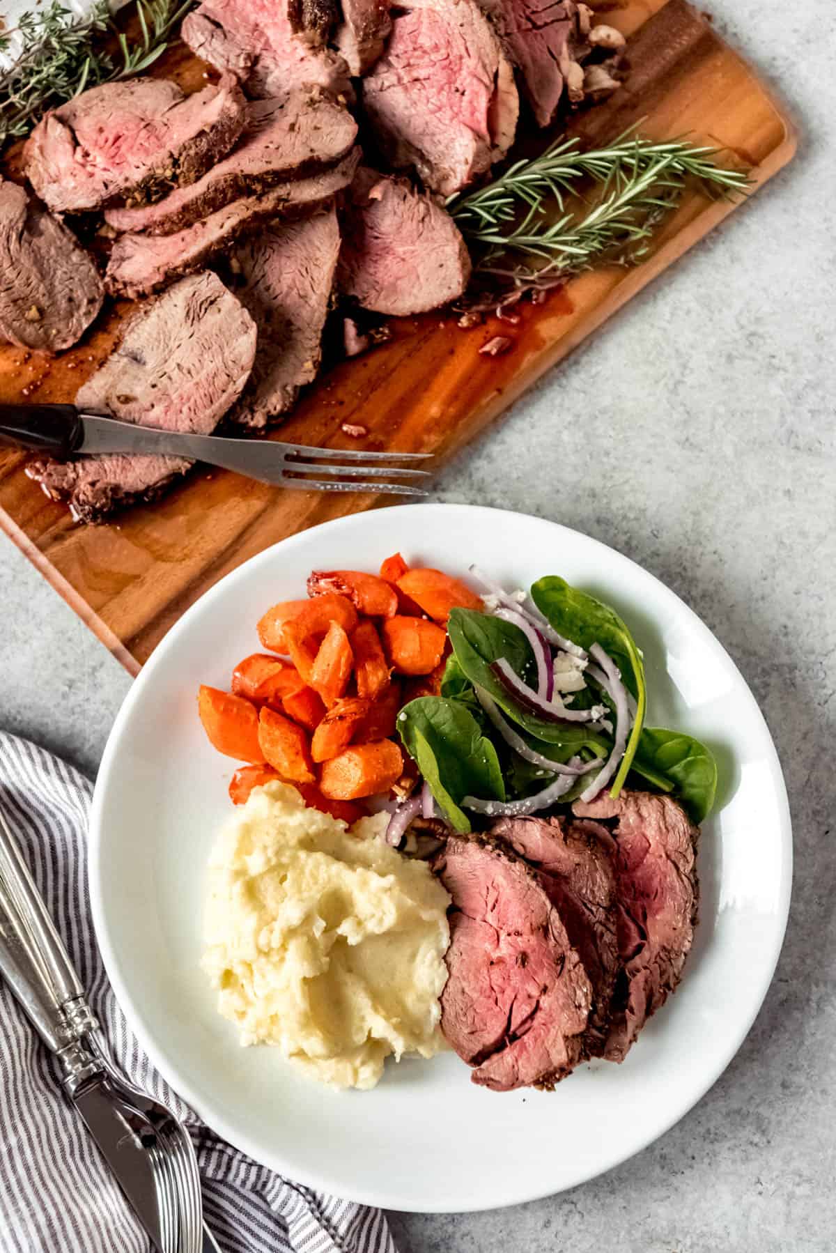 Top view of a plate of sliced beef tenderloin with creamy mashed potatoes, roasted carrots, and salad.