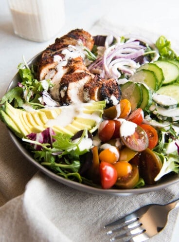 Grilled Cajun Chicken Salad ingredients all in a bowl with dressing drizzled over the top.