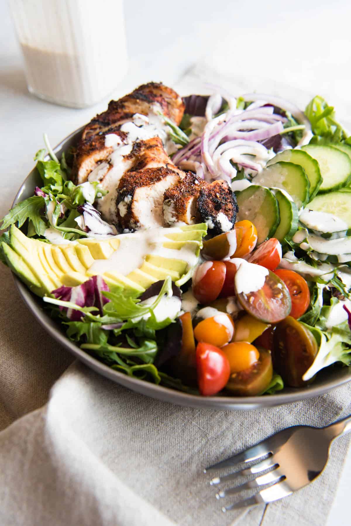 Grilled Cajun Chicken Salad ingredients all in a bowl with dressing drizzled over the top.
