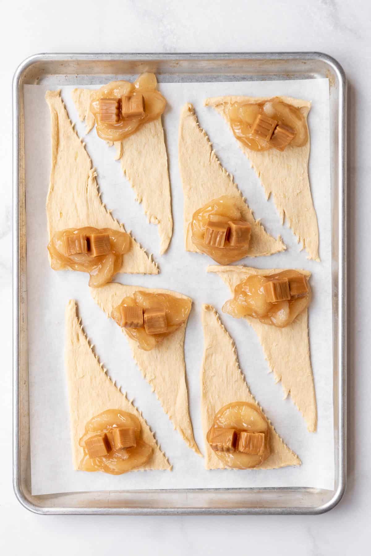 Triangles of crescent roll dough with apple pie filling and caramel squares on top.