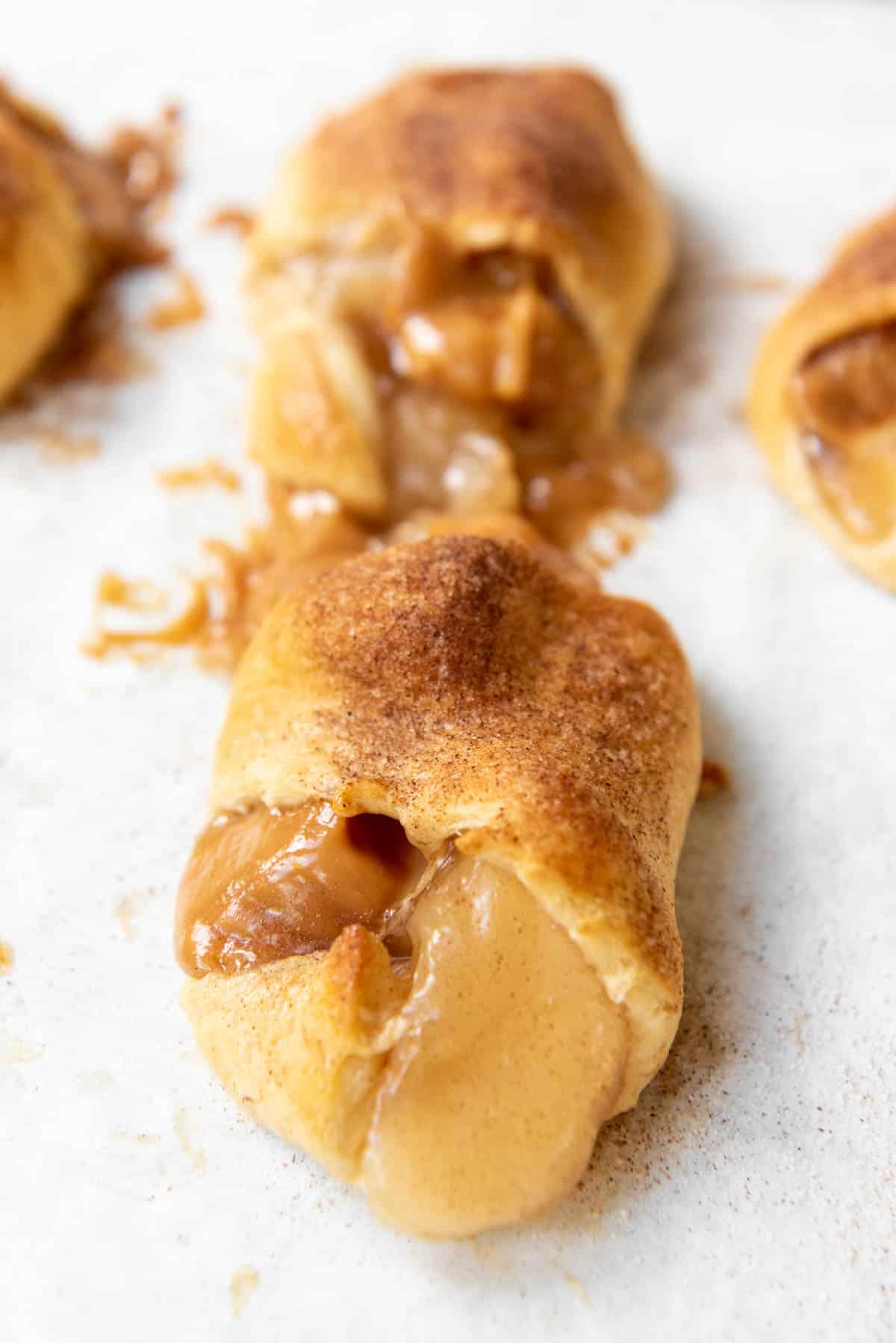 A side angle of apple slices and caramel spilling out of a baked Pillsbury crescent roll.