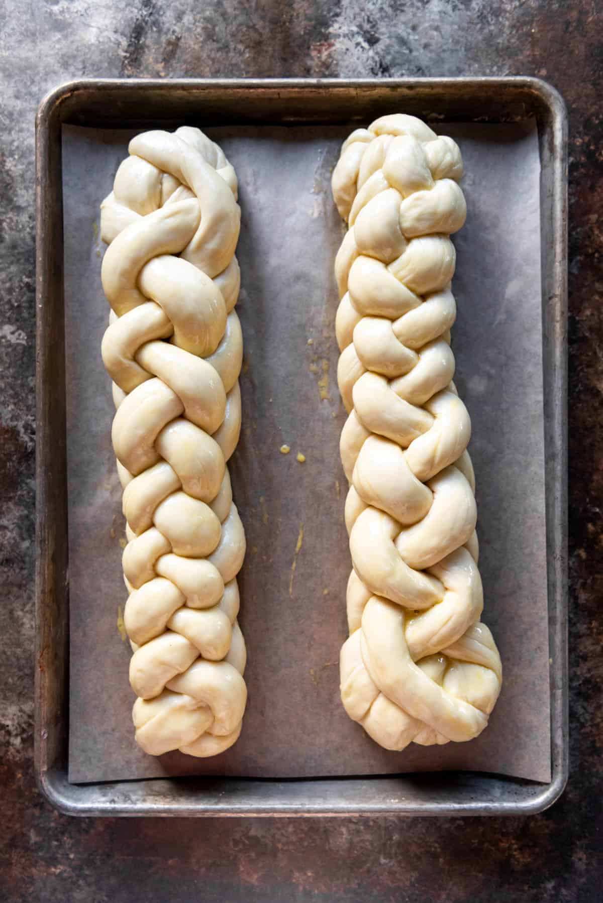 An image of two unbaked loaves of challah bread that have been brushed with egg wash.