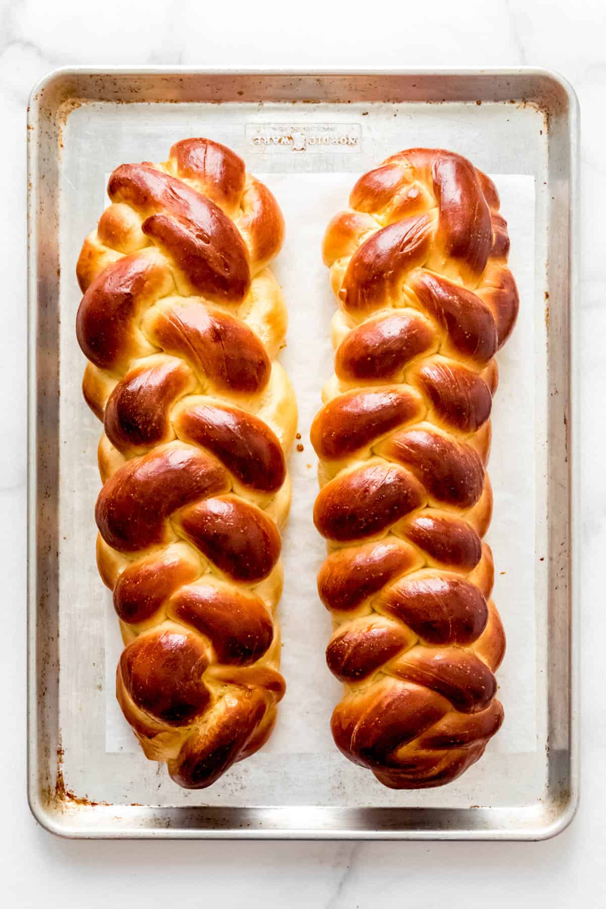 Two loaves of braided challah bread on a baking sheet.