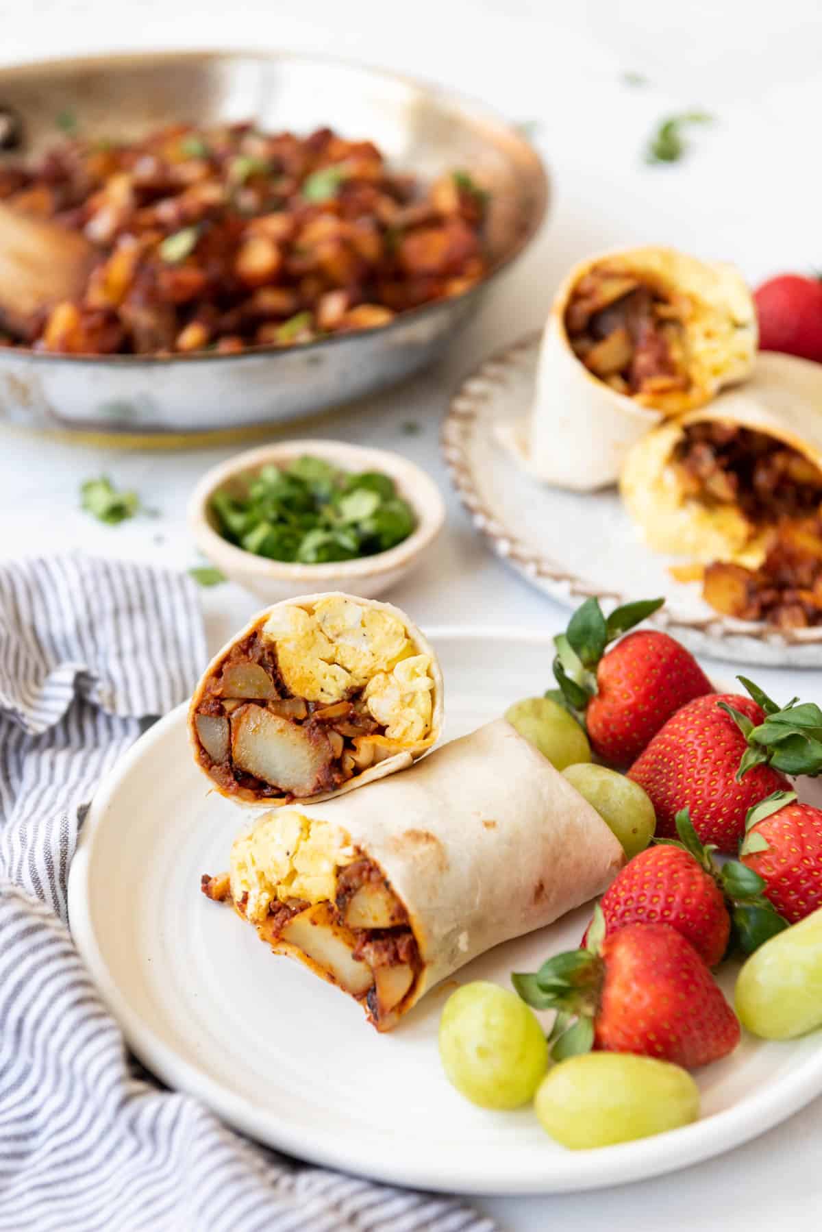 Potato and chorizo wraps on a white pate with fresh fruit. 