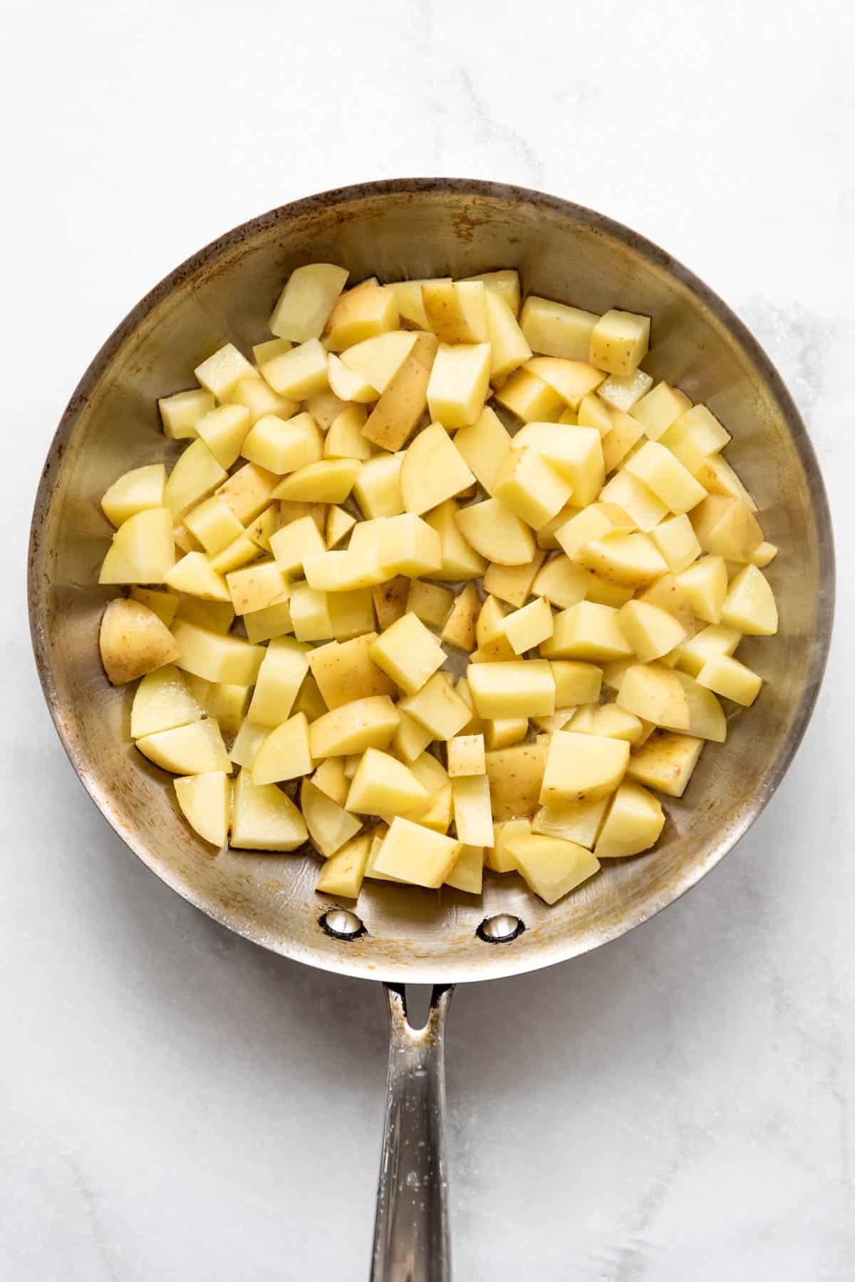 Top view of a frying pan with diced potatoes in it. 