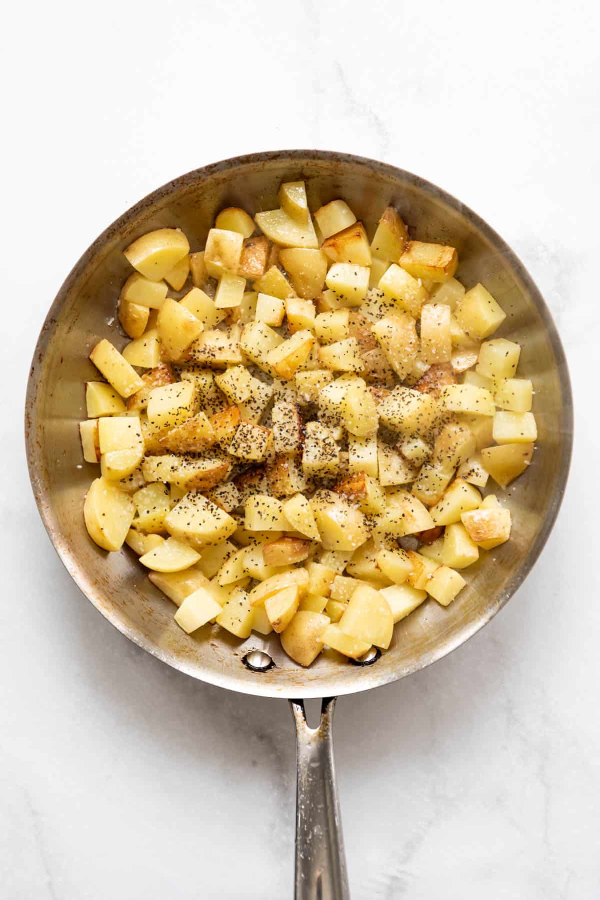 To view of a frying pan with diced potatoes and seasoning in it. 