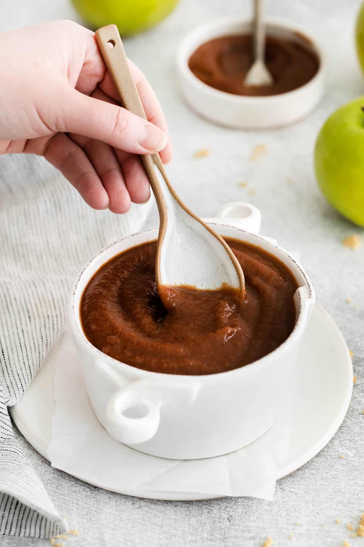 A hand holding a spoon over a bowl of homemade crockpot apple butter.