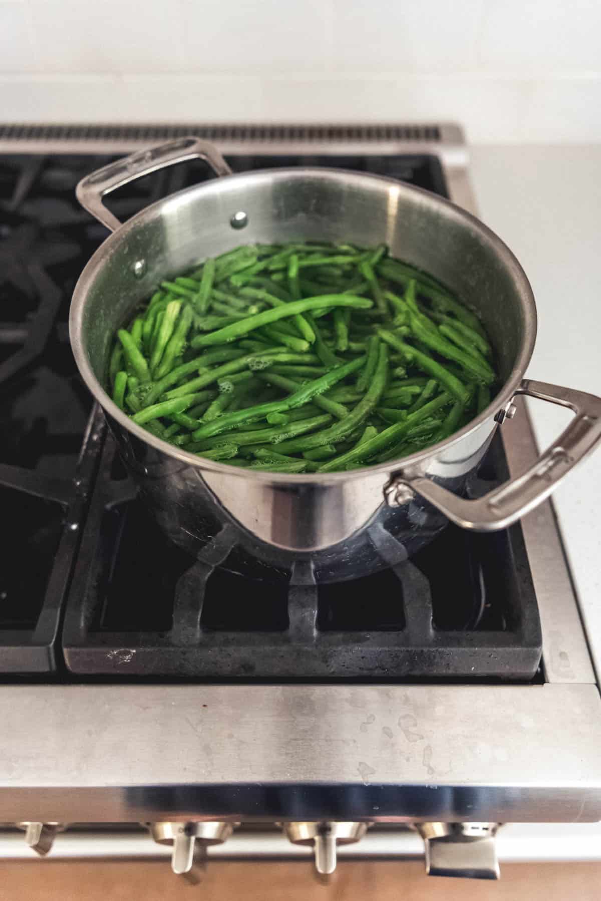 A pot of boiling water on the stove with fresh green beans.