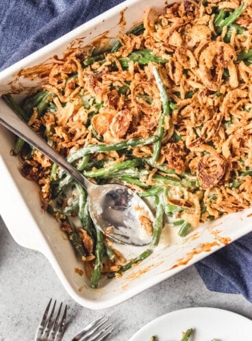 A close up of a white baking dish with green bean casserole and a serving spoon inside.