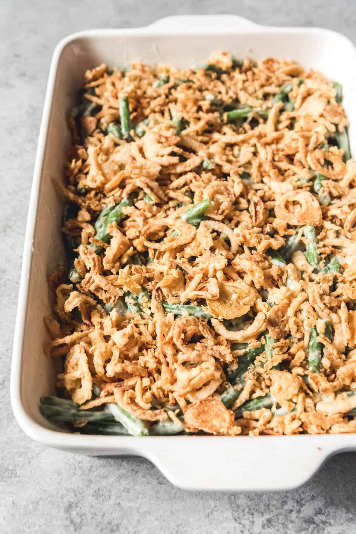An image of a classic green bean casserole topped with fried onions before going into the oven to bake.
