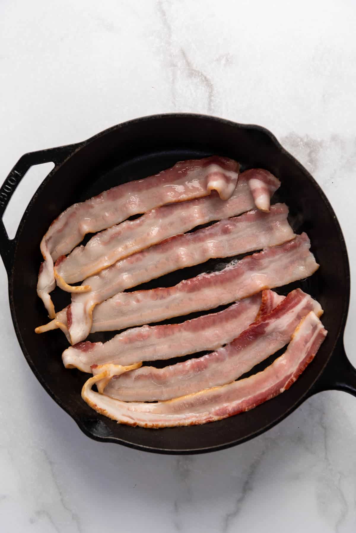 Frying bacon slices in a cast iron skillet.