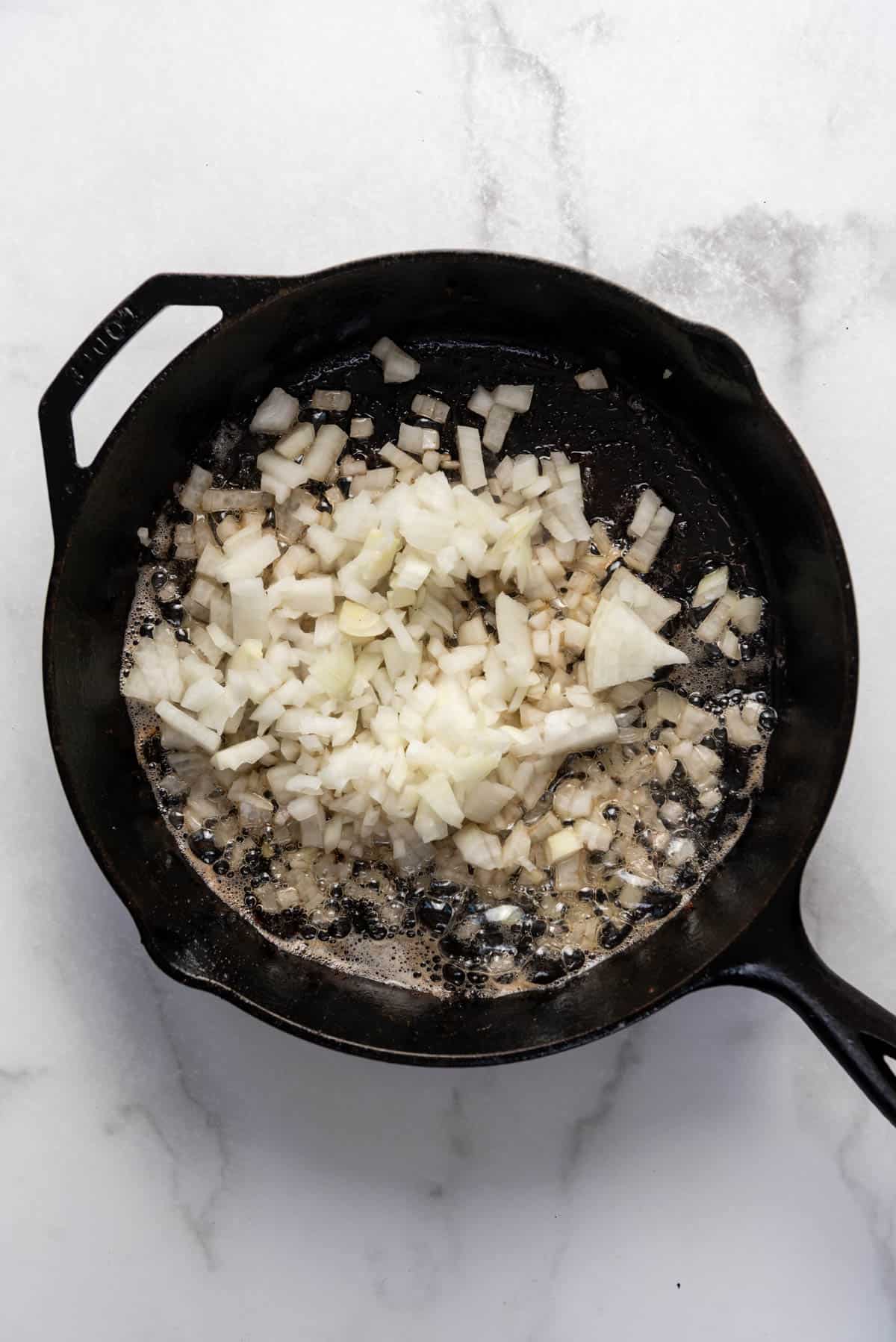 Chopped onions being sauteed in bacon grease in a cast iron skillet.