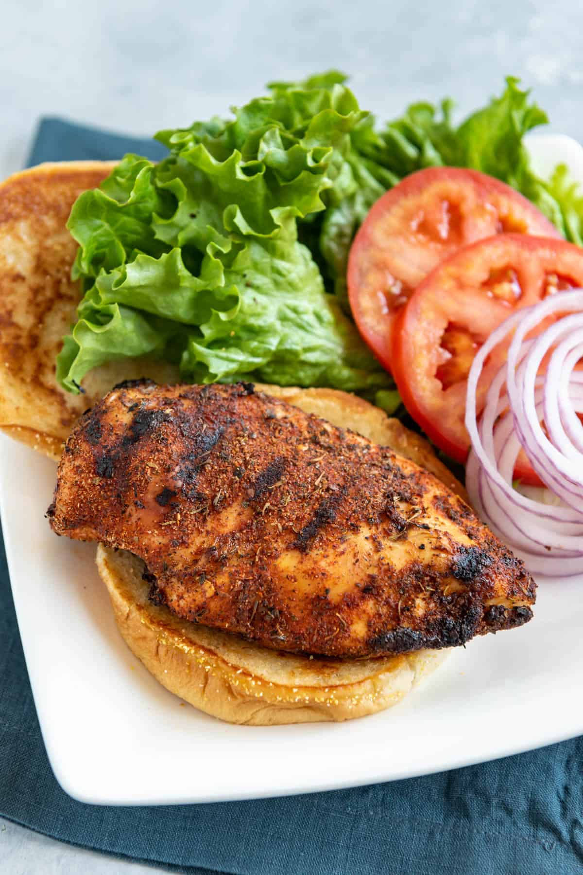 Grilled Cajun chicken on a burger bun with lettuce tomatoes and sliced red onions.