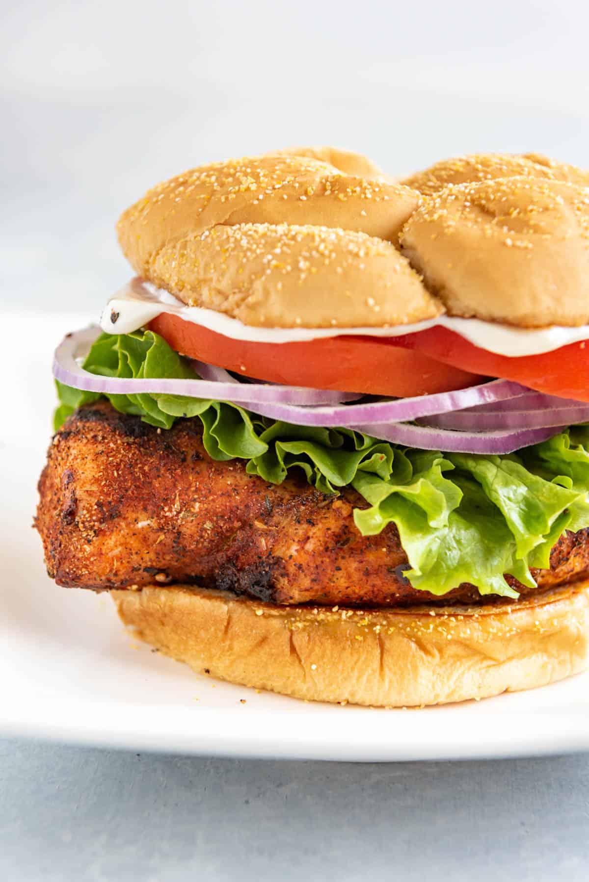 A grilled Cajun chicken sandwich with lettuce red onions tomatoes and sauce.