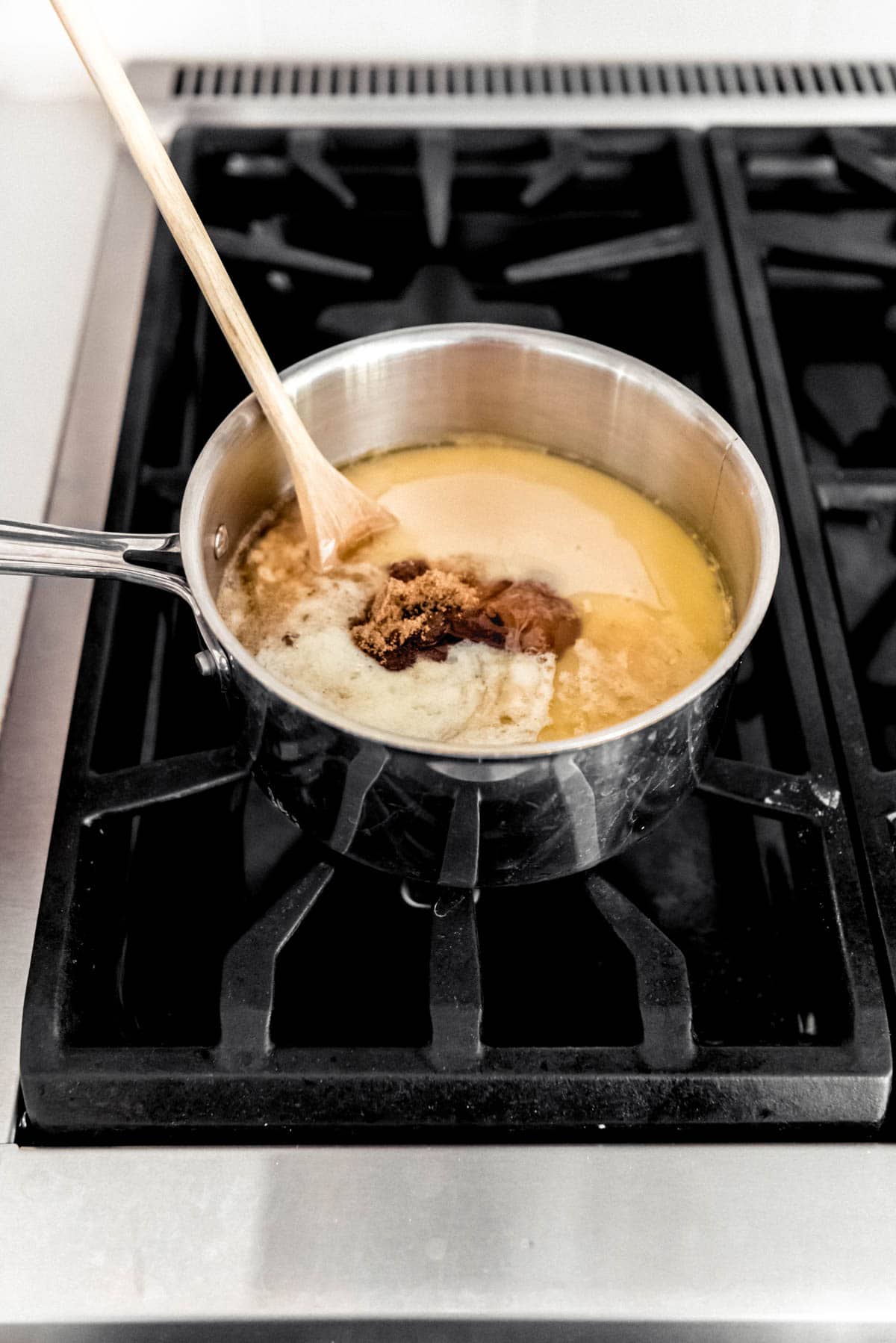 Adding sweetened condensed milk and brown sugar to melted butter in a saucepan on the stove.