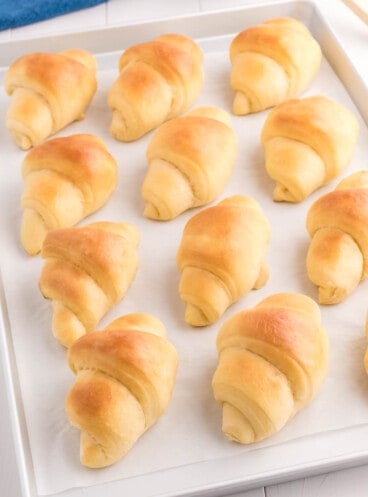 Homemade crescent rolls lined up on a baking sheet.