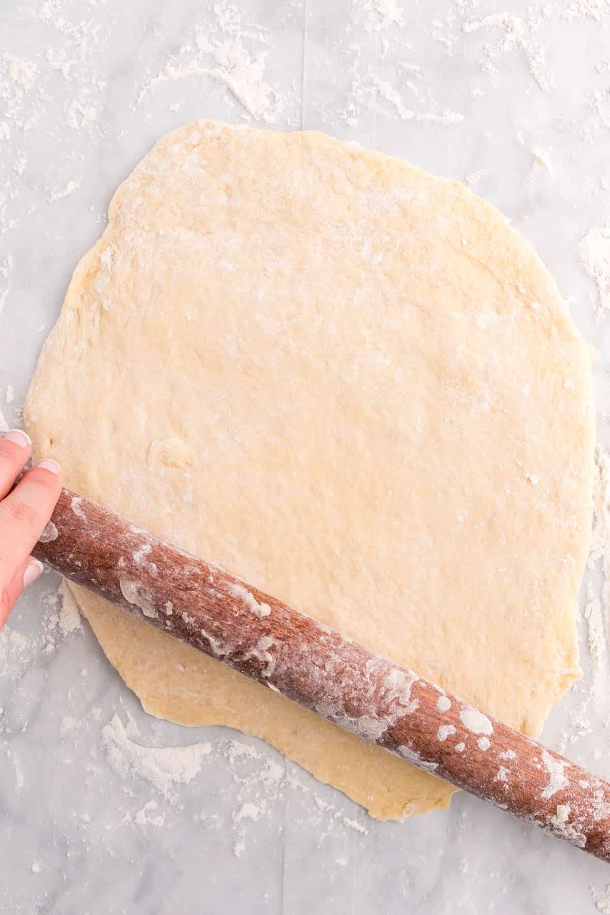 Top view of dough being rolled out on a floured surface with a rolling pin. 