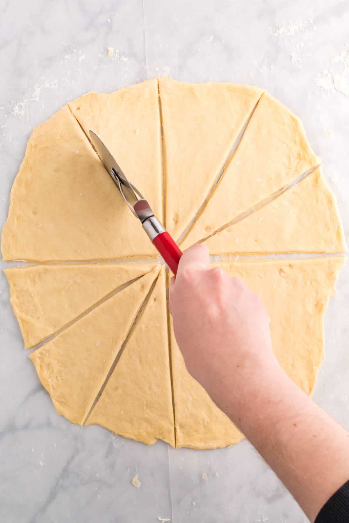 Top view of rolled out dough being cur into triangle segments wth apizza cutter. 