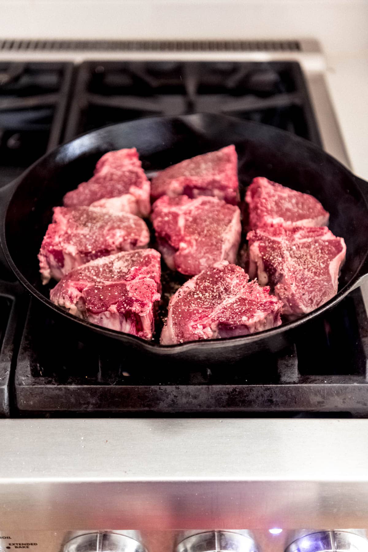 A skillet on the stove filled with seasoned lamb chops.