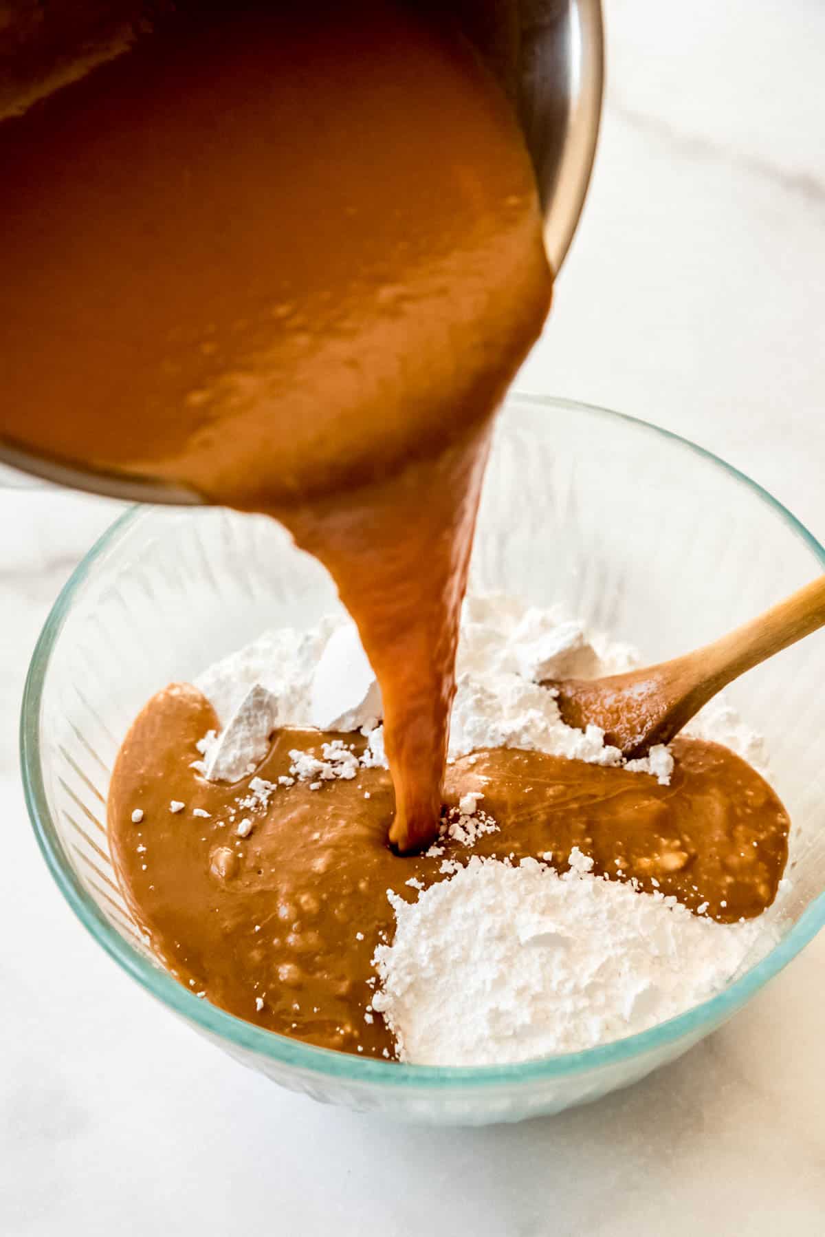 Close up of peanut butter fudge mixture getting poured into a glass bowl to mix with powdered sugar.