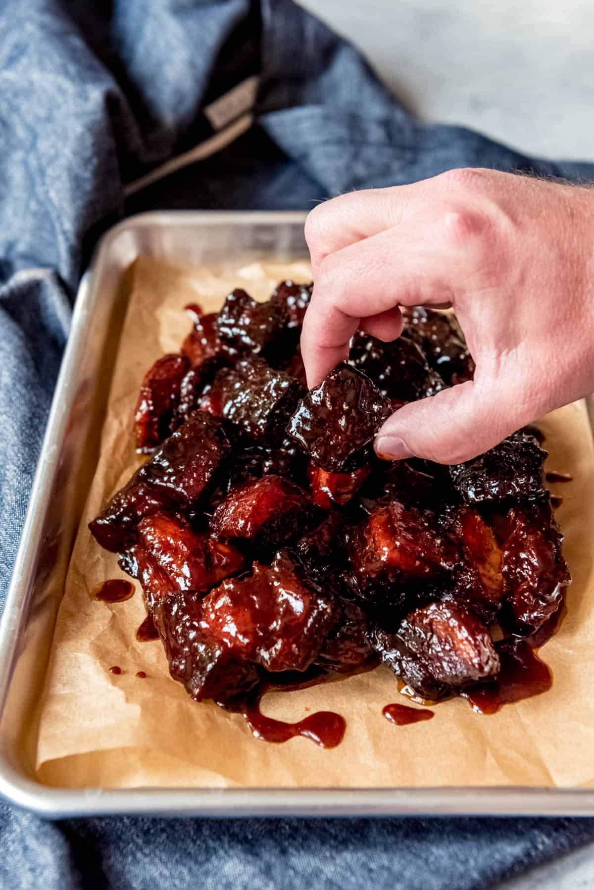 An image of a hand picking up a cube of smoked pork belly burnt ends.