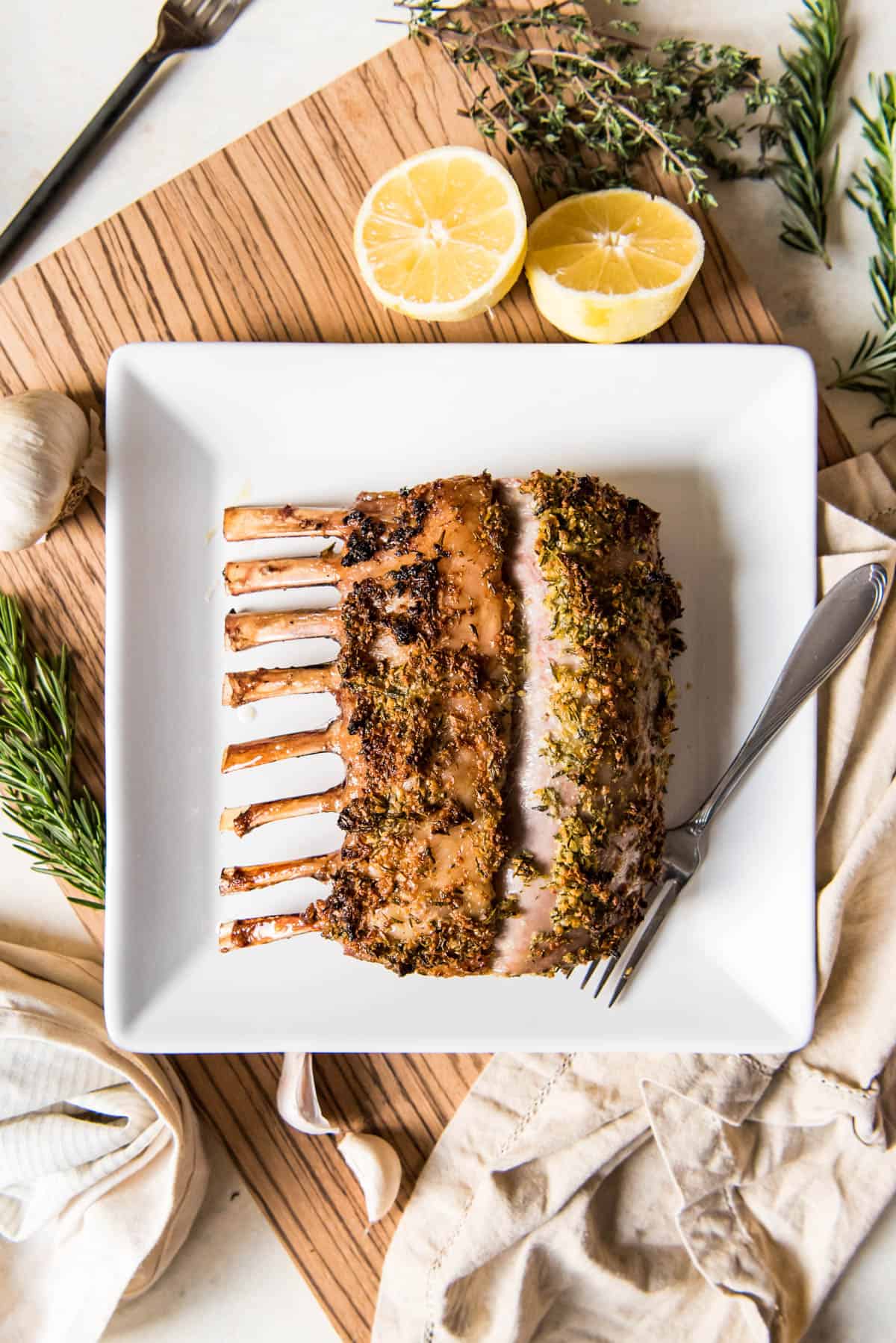 Cooked rosemary garlic rack of lamb on white plate with fork.