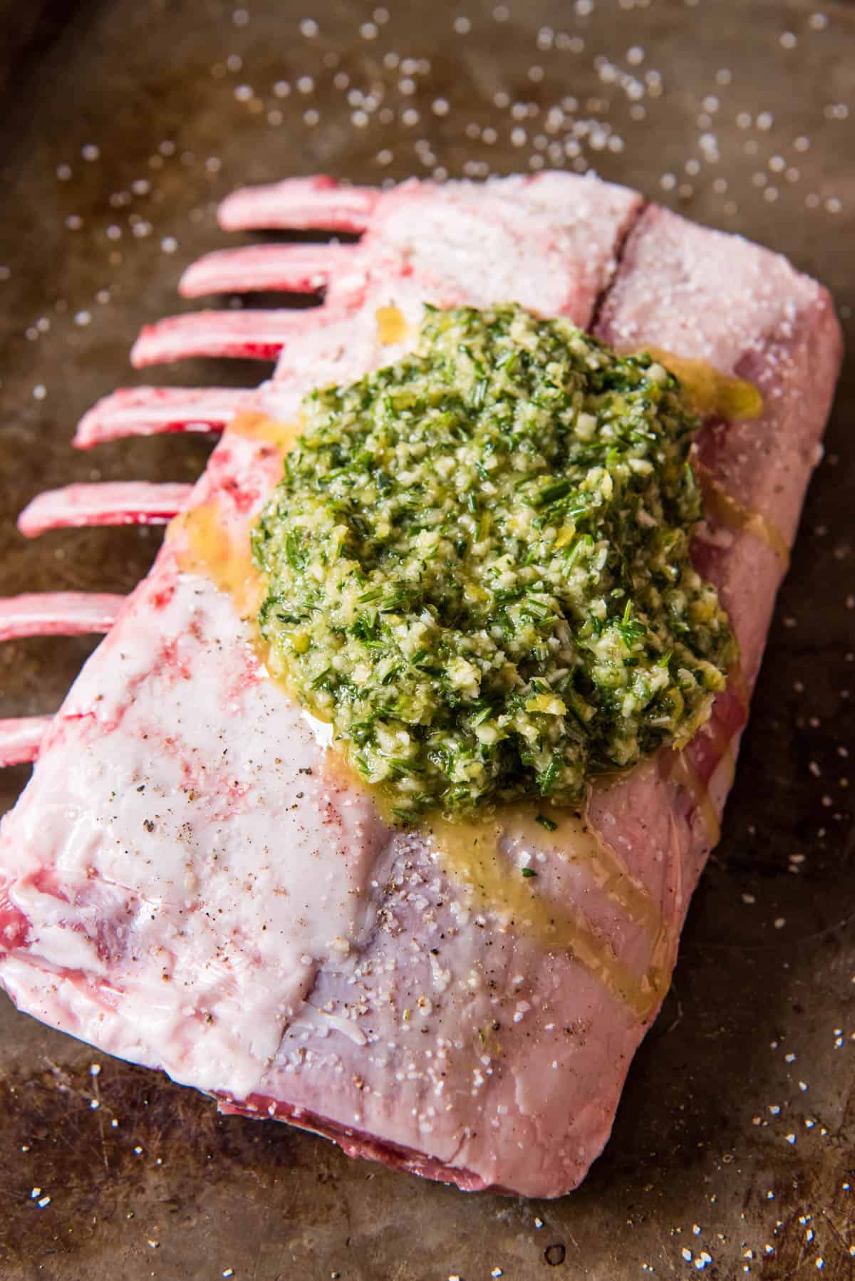 Rack of lamb fat side up with a marinade of olive oil, lemon zest, garlic, rosemary and thyme ready to be rubbed on it.