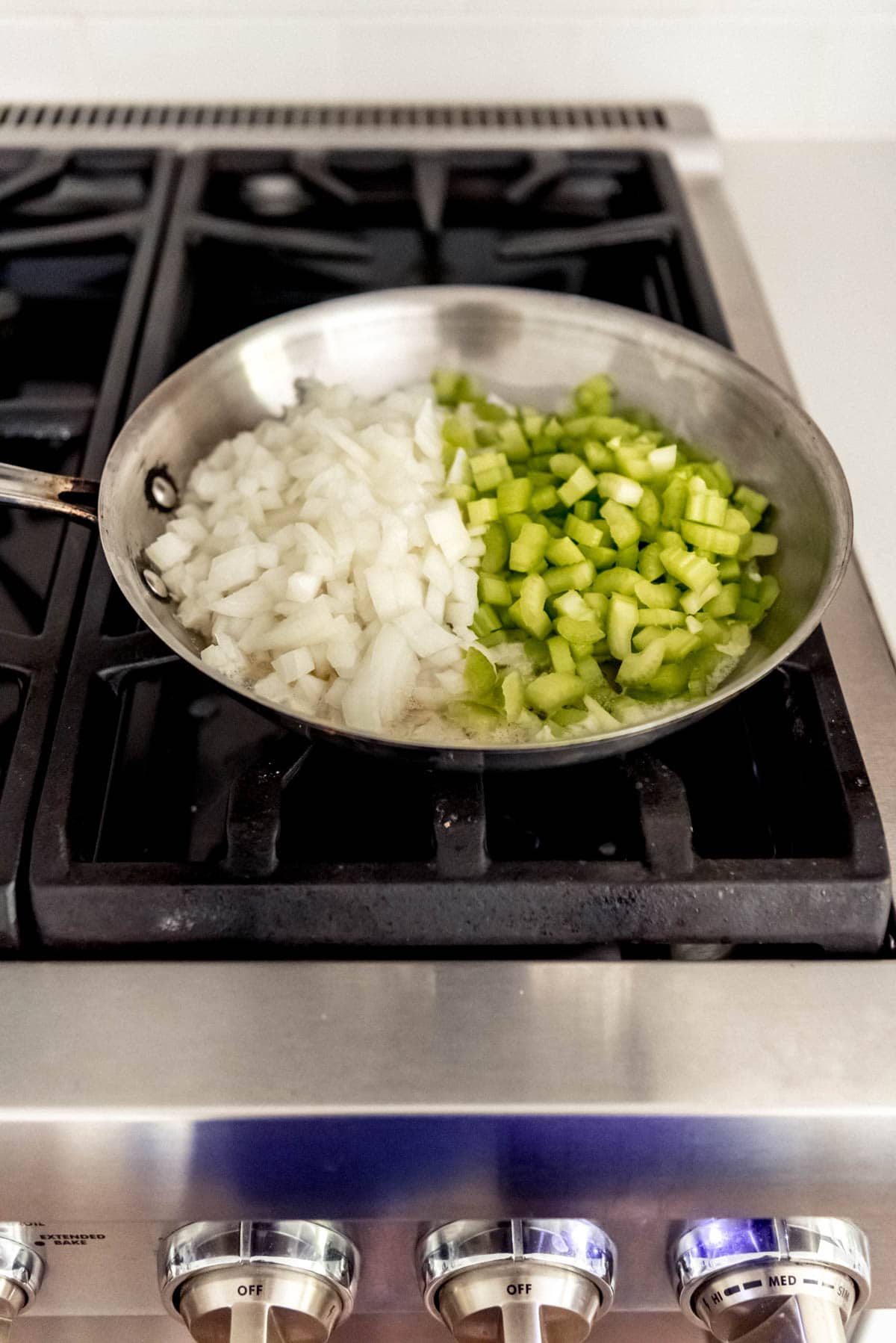 Chopped celery and onions in a pan on a stove.