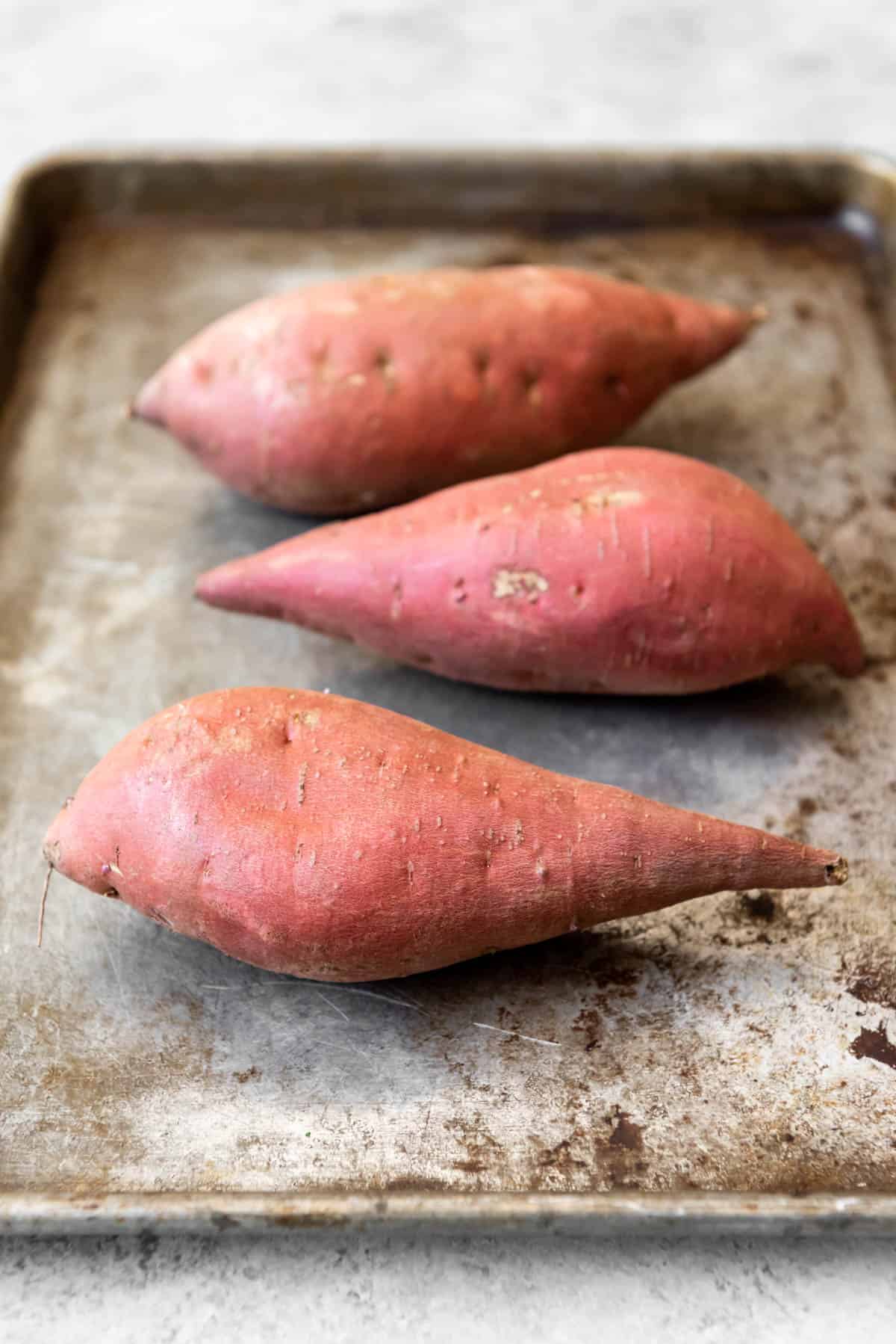An image of sweet potatoes in their skins on a pan for roasting in the oven.