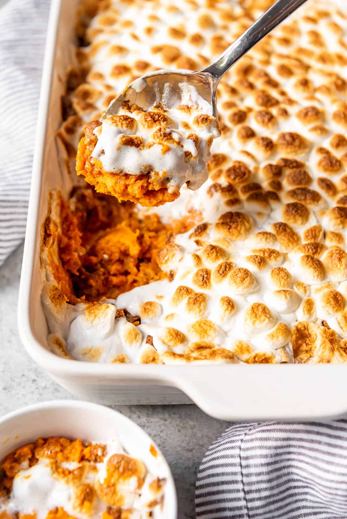 Sweet potato casserole with marshmallows in a white baking dish with a spoon scooping some out of the pan.