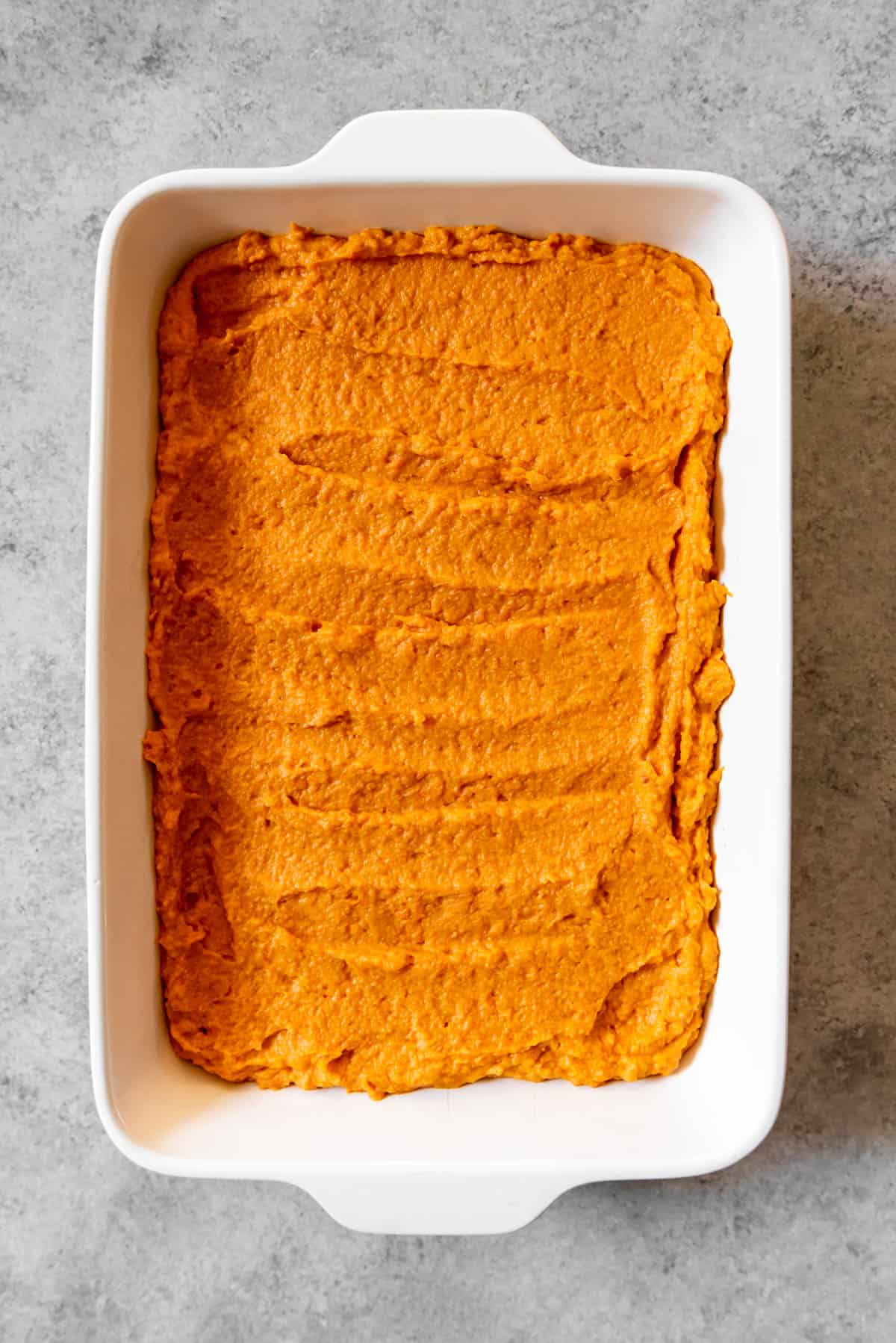 An image of mashed sweet potatoes with brown sugar, milk, butter, and cinnamon in a serving dish, ready to be topped with marshmallows for sweet potato casserole.