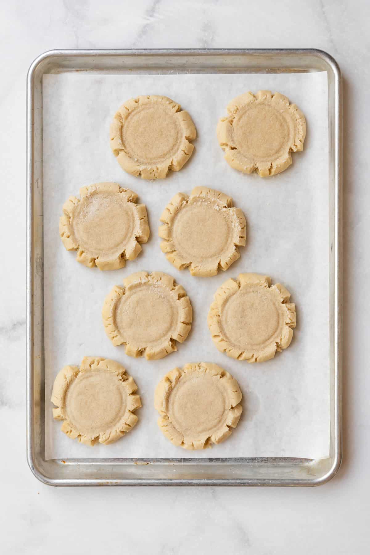 A baking sheet with eight round sugar cookies with jagged edges.