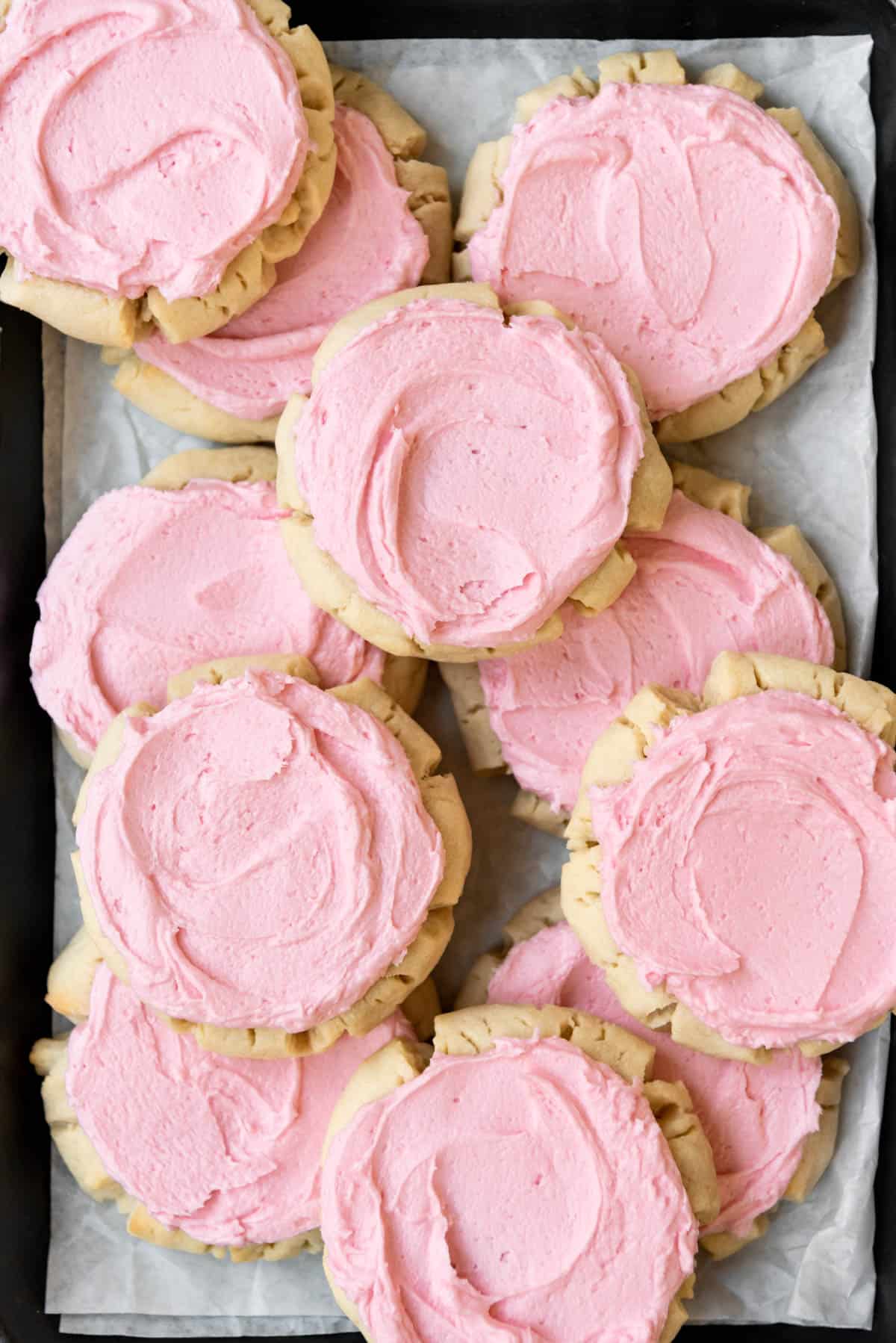 A close image of swirls of pink frosting on soft sugar cookies.