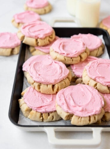 Pink frosted sugar cookies on a platter in front of glass jars of milk.